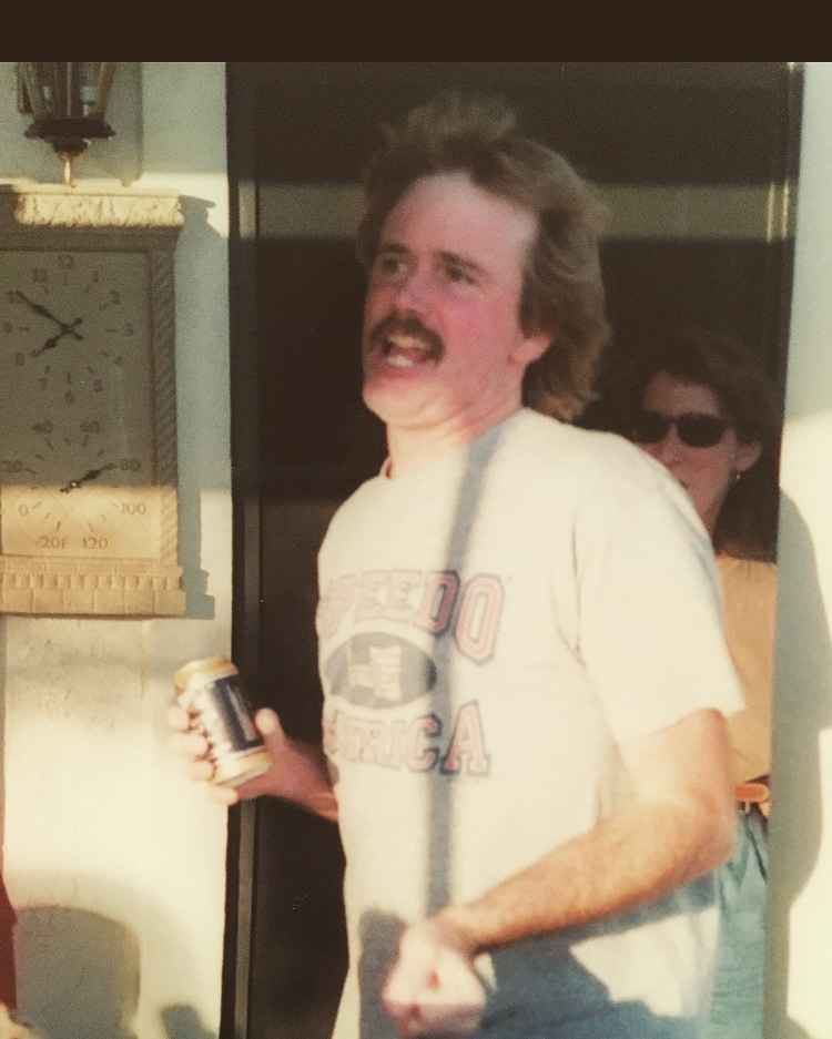 Father holding a beer can; a wall clock and a woman with sunglasses stand behind him.