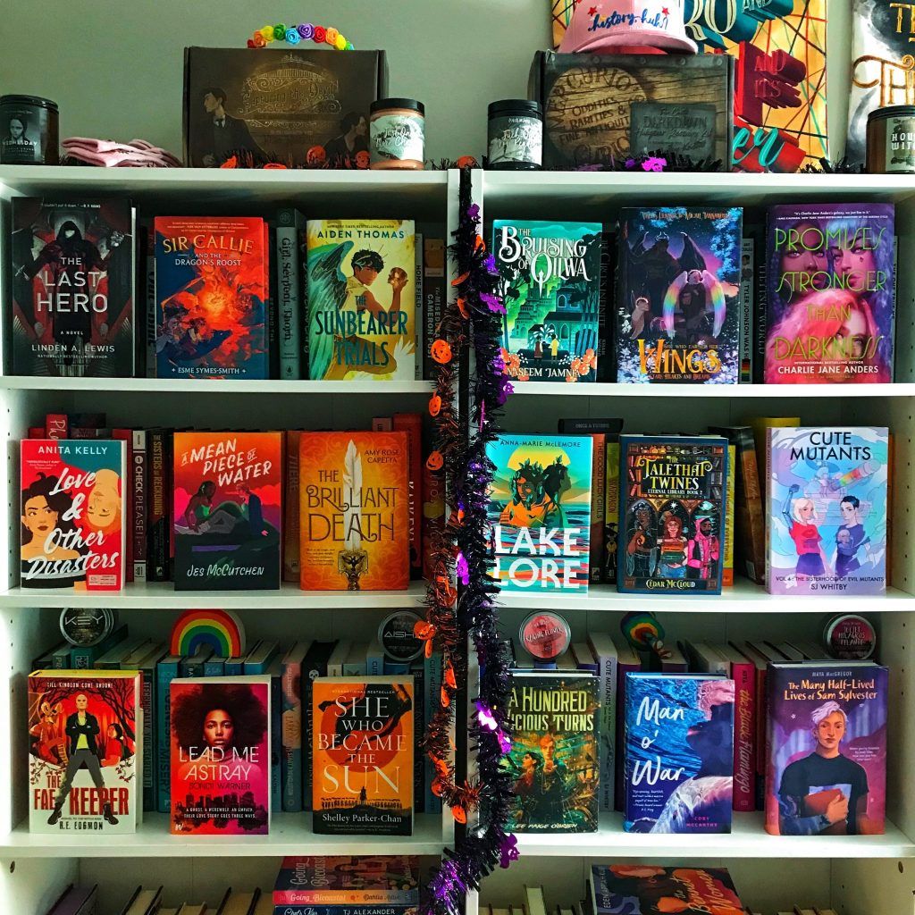 White bookshelves filled with colorful books, knick-knacks on top, and Halloween-themed tinsel garlands running down between bookcases.