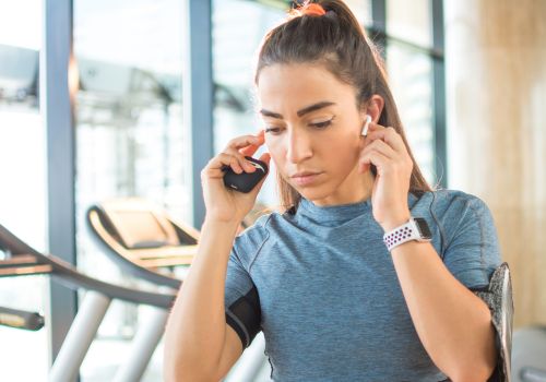 A woman in the gym raising both hands to her ears to adjust her earphones.