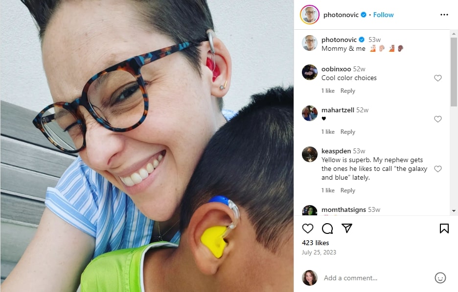 Instagram post showing a photo of Sara Novic with a child (face hidden). Both are wearing colored ear devices.