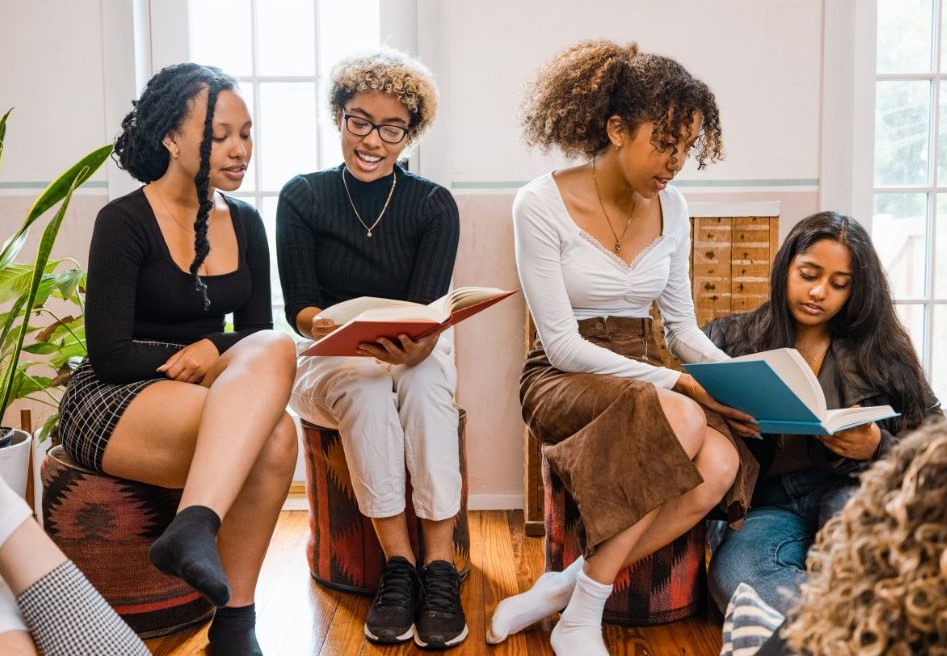 Four women sitting around reading books together.