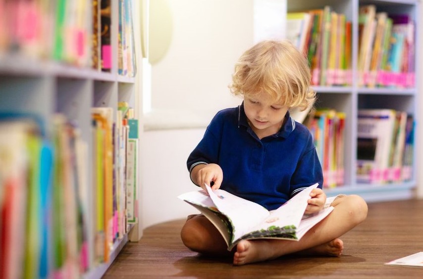A young child reading near full bookshelves.