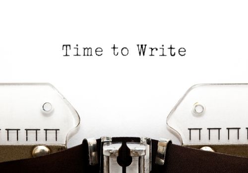Close-up of a typewriter with words "Time to Write" written in black ink on a white page.