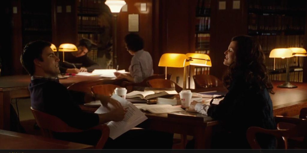 Two college friends are studying at a table in the library with books and coffees.