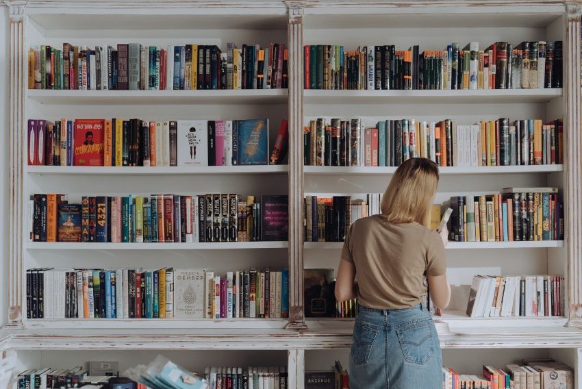 A person pulling a book off of a packed bookshelf