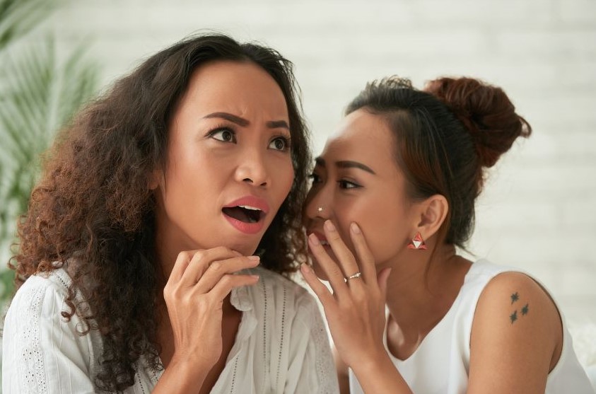 A woman whispering something to a shocked woman