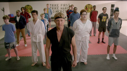 Cobra Kai still with Johnny Lawrence in the front and center dressed in his all black karate gi. Students form behind him in ready position awaiting instruction.