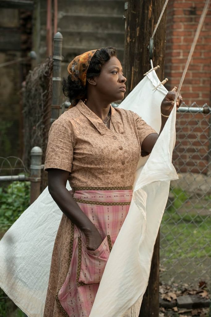 Actress Viola Davis stands by a fence, gazing out at the street. She is hanging clothing on a line.