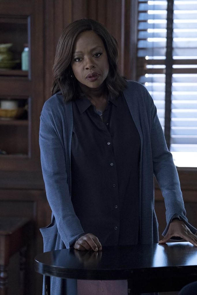 Viola Davis as Annalise Keating stands at a table, gazing pensively down.