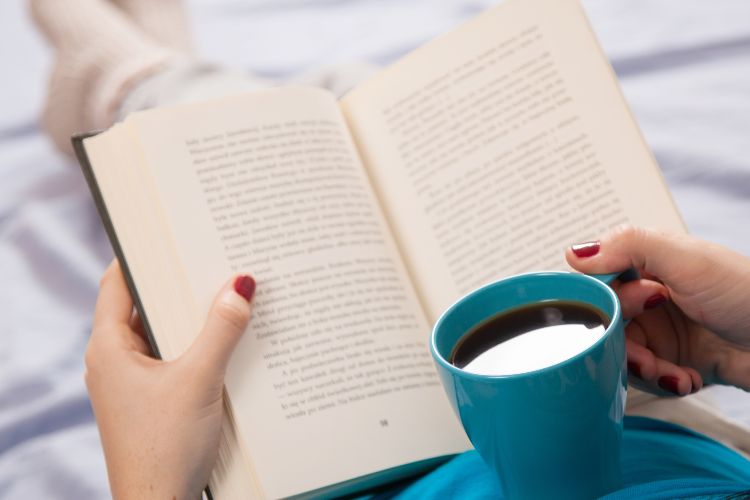 A person reading a book with a cup of coffee in their hand.