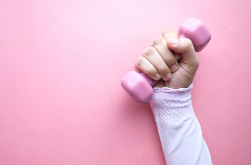 A hand lifting a small pink dumbell.