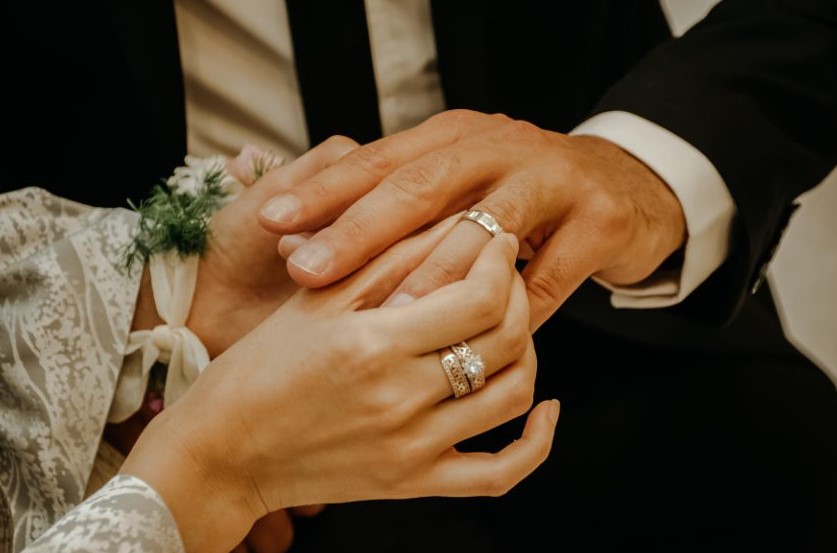 Someone sliding a wedding ring onto their new spouse's finger.