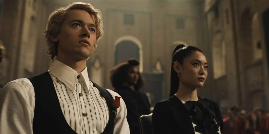 A bottom-up view of man with curly blonde hair in a white and black button up shirt and black vest next to a woman with a sleek black ponytail.