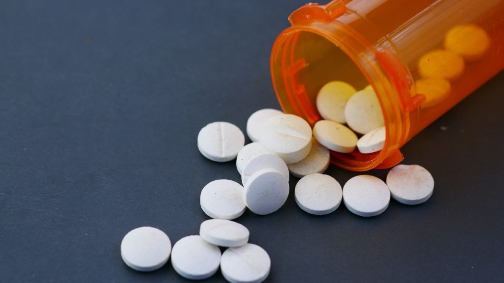 A tipped over pill bottle containing round white pills on a blue surface.
