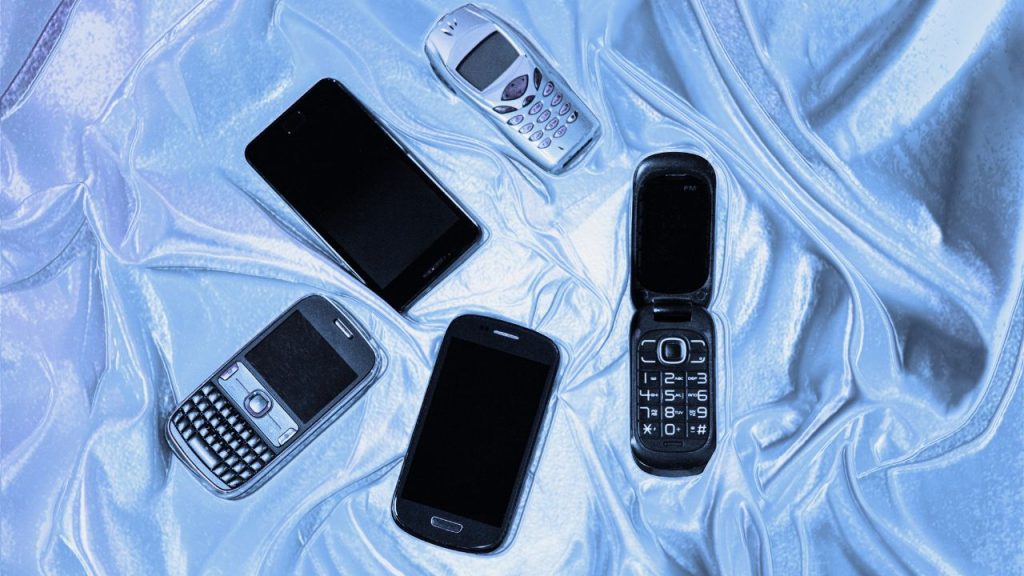 Five phones - a mix of flip phones and smart phones - sitting on a weird satiny light blue textured surface.