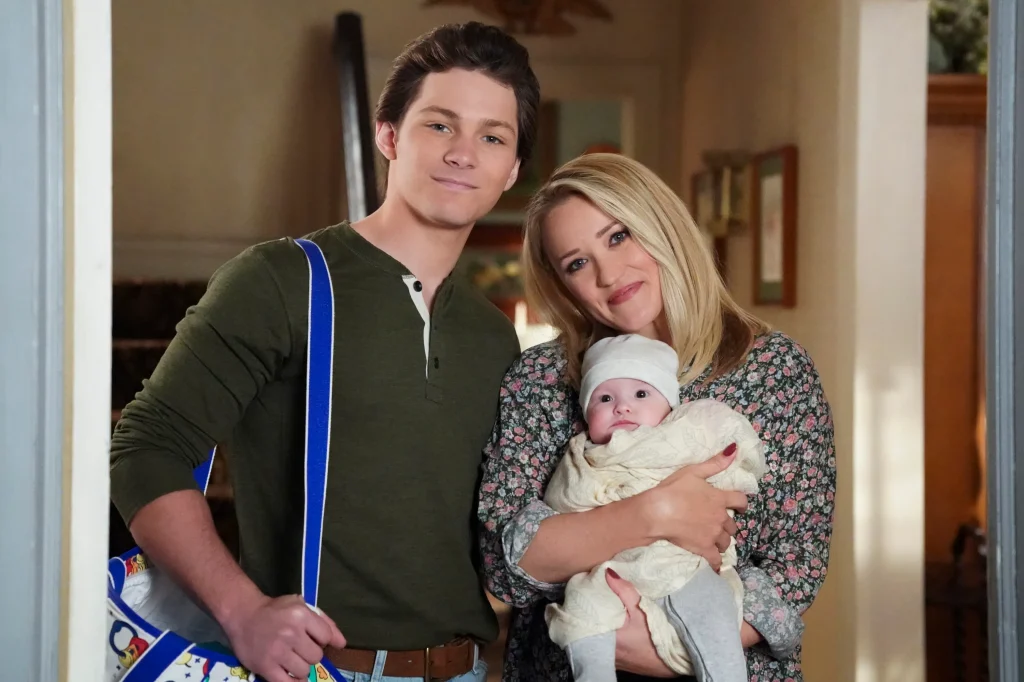 Montana Jordan and Emily Osment stare at the camera, holding a baby.