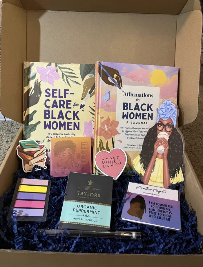 Self-care box featuring a book on Black women's self-care, a journal, stickers, and a pen. The box is neatly arranged, showcasing its contents.