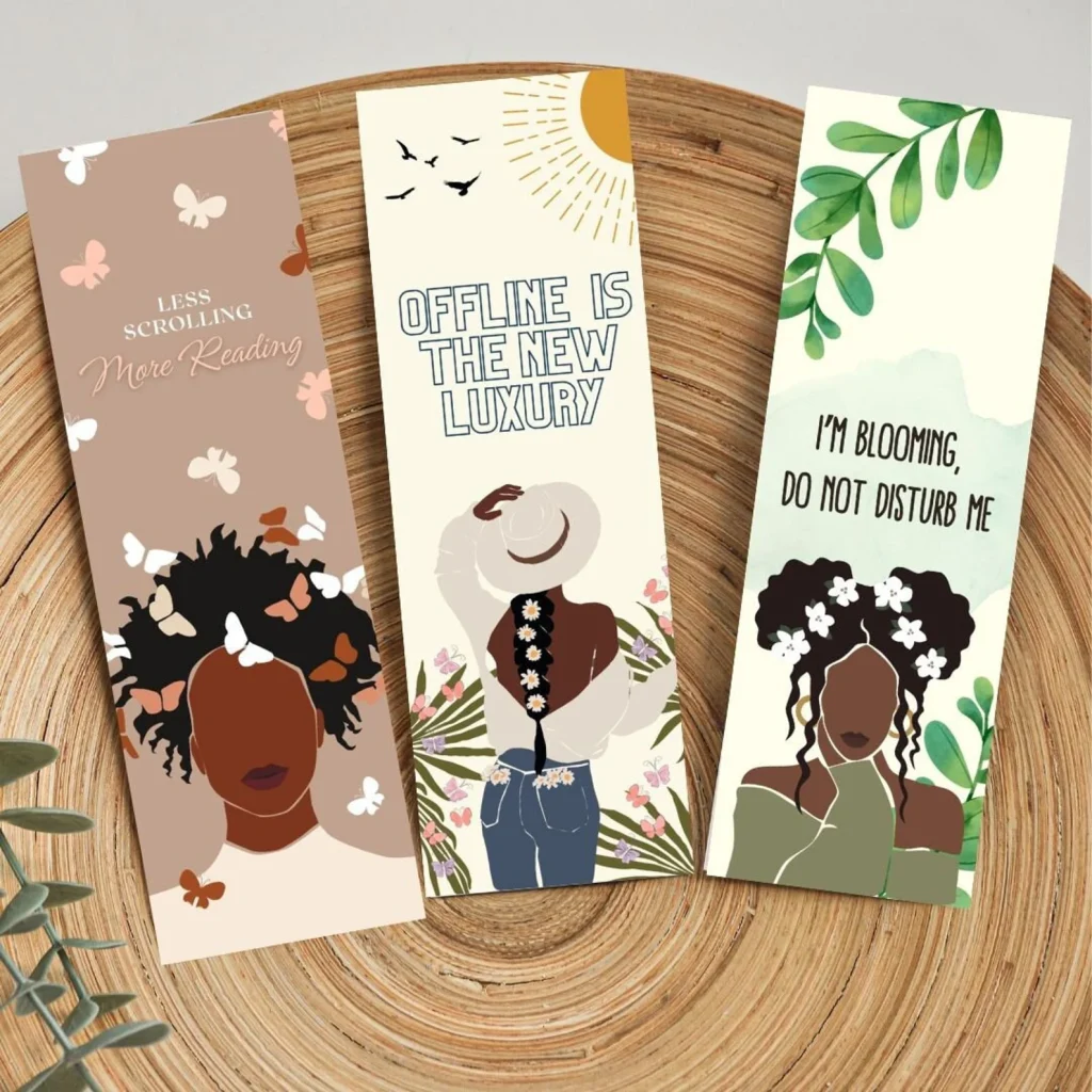 Three bookmarks, each featuring a different Black woman in various poses against a motivational background. Each bookmark has a distinct design and phrase, reflecting empowerment and inspiration. The women are depicted in vibrant colors and styles, adding a personal touch to each bookmark.