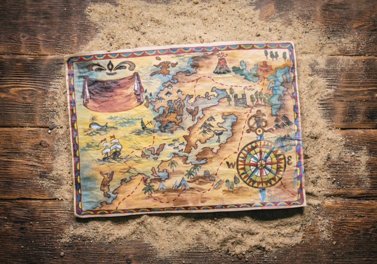 An old-looking colourful map on top of a pile of sand on a wooden surface.