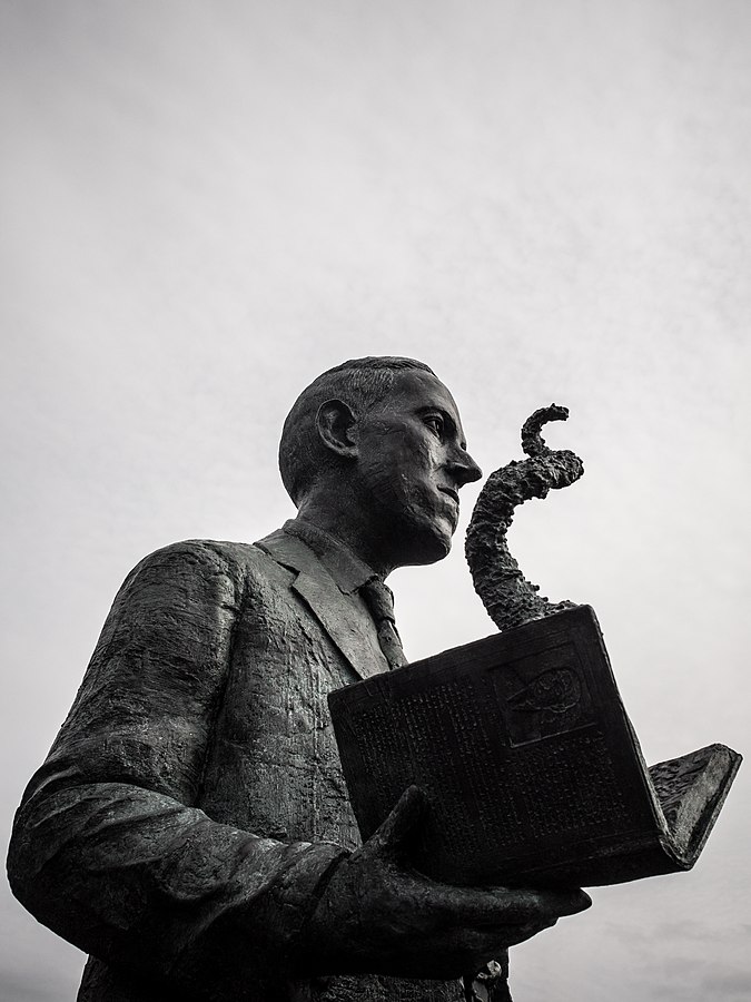 Black and White of a statue of H.P. Lovecraft holding an open book with a tentacle coming out of it.