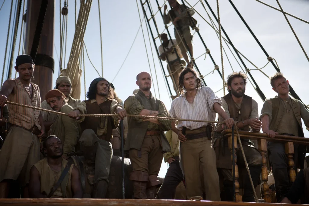 A group of crew members standing around and peering over the side of a pirate ship.