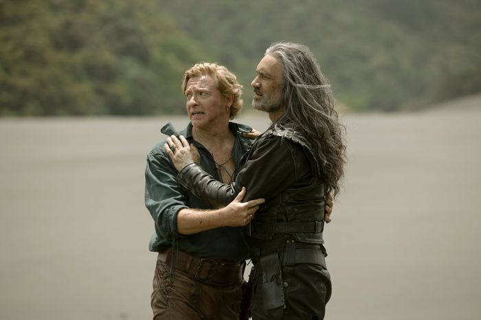Stede and Ed standing on a beach and embracing each other as they speak to someone outside of the frame.