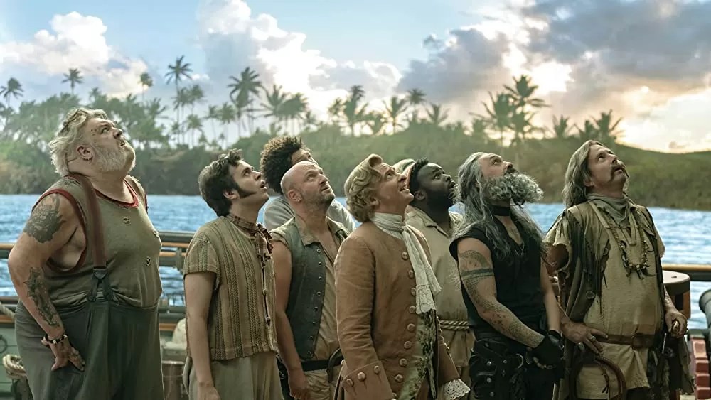 The crew of the Revenge standing on the deck of a ship and looking up at the sky. In the background, tall palm trees and large white clouds litter the sky.