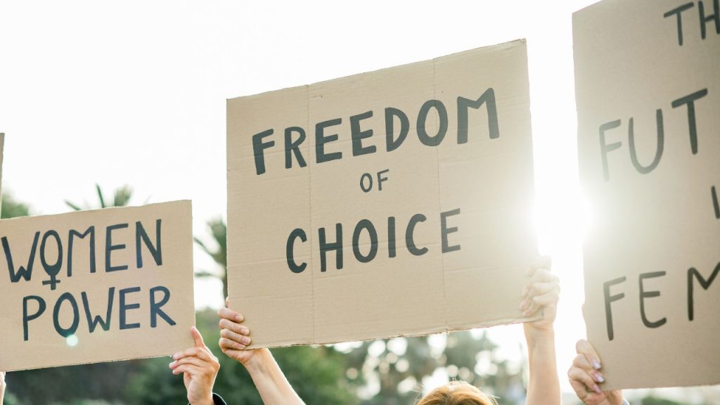 Hands holding signs that say 'women power', 'freedom of choice' and 'the future is female'.