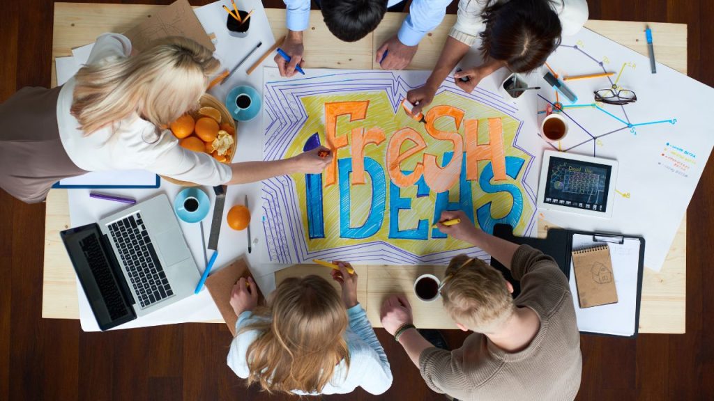 A bird's-eye view of a group of people designing a poster that reads "Fresh Ideas."