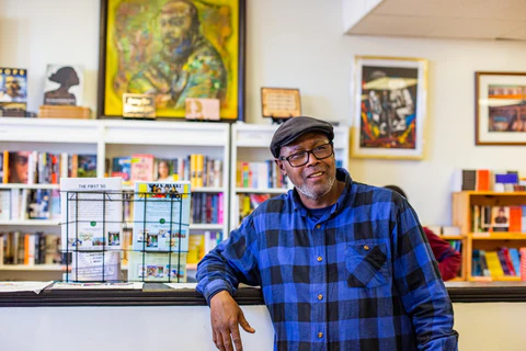 A content-looking man stands in a bookstore with artwork hanging on the wall.