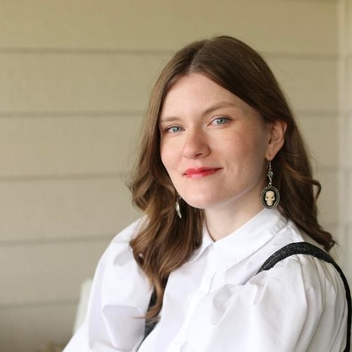 Sophia smiling at the camera while wearing a white collared top and skull earrings