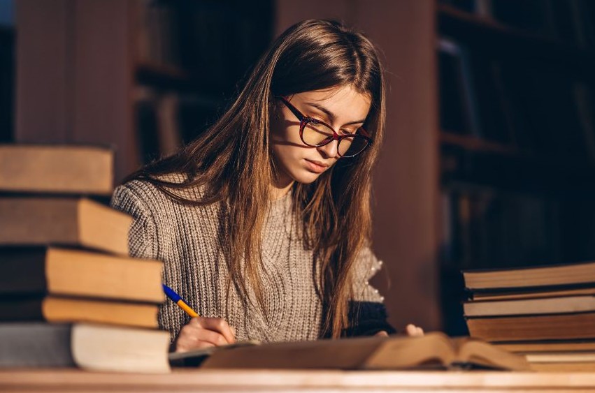 A woman surrounded by books while writing something
