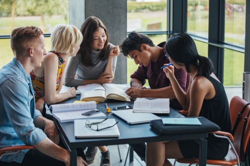 Five people gathered around a table full of open books