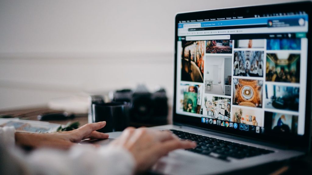 Hands typing on a laptop open to a tab full of photos.