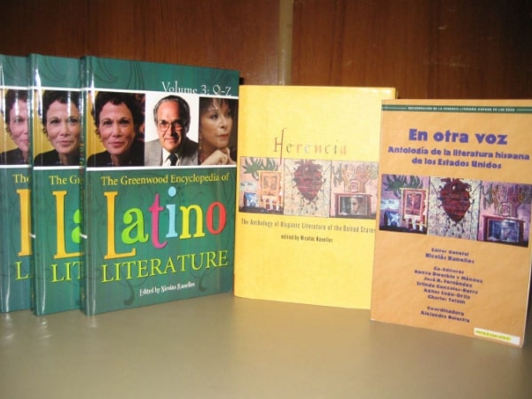 A collection of books published by Arte Público Press, including 'The Greenwood Encyclopedia of Latino Literature' and 'Herencia: The Anthology of Hispanic Literature of the United States.' The books are displayed on a wooden shelf, reflecting the publisher's dedication to Hispanic literature and culture