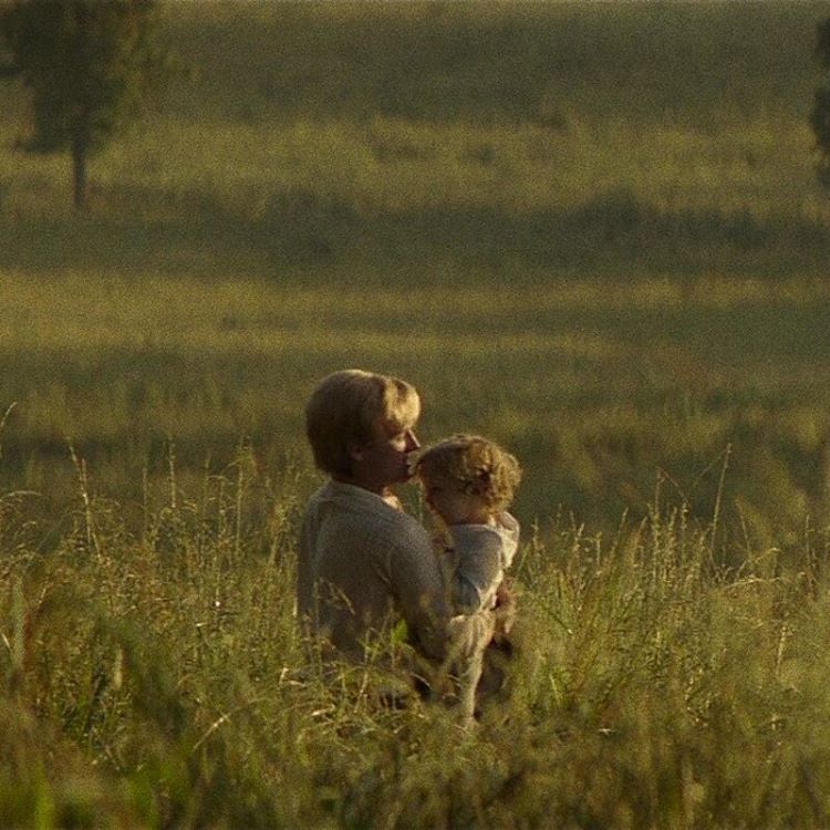 A green field with a man (Peeta) holding his son