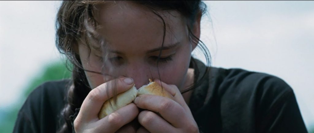 A young girl (Katniss) sniffing a piece of bread