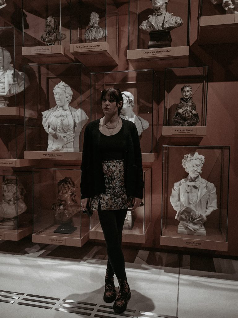 Full body picture of bookstagrammer of the week, Vicky, posed in front of a wall of sculptures.