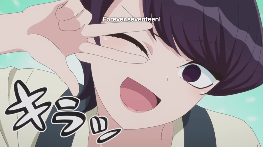 "Komi-san Can't Communicate" anime shot of Shuuko Komi introducing herself to Tadano, winking with her hands over her closed eye. The subtitles on the top say "Forever seventeen!"