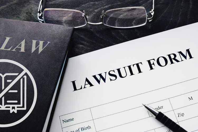 blank lawsuit form and law book on a table next to reading glasses.