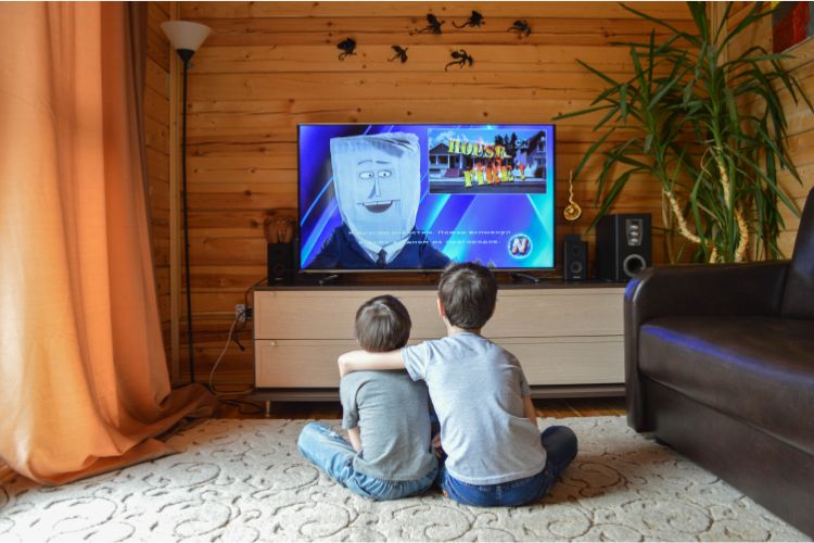 two young kids in front of the TV. The one on the right has an arm around the other