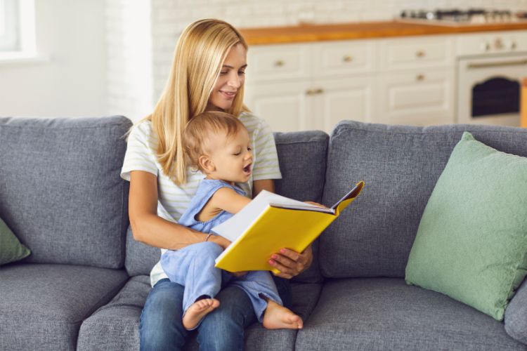 woman sitting on a couch with her child on her lap. showing child a book with yellow cover
