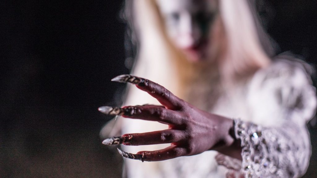 Canva image of a woman in white clothing blurred in the background with her hand clear with long nails with metal designs.