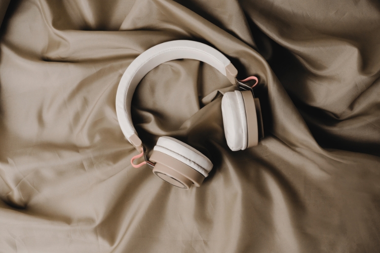 A pair of brown and white over-the-ear headphones sits on a rumpled brown sheet.
