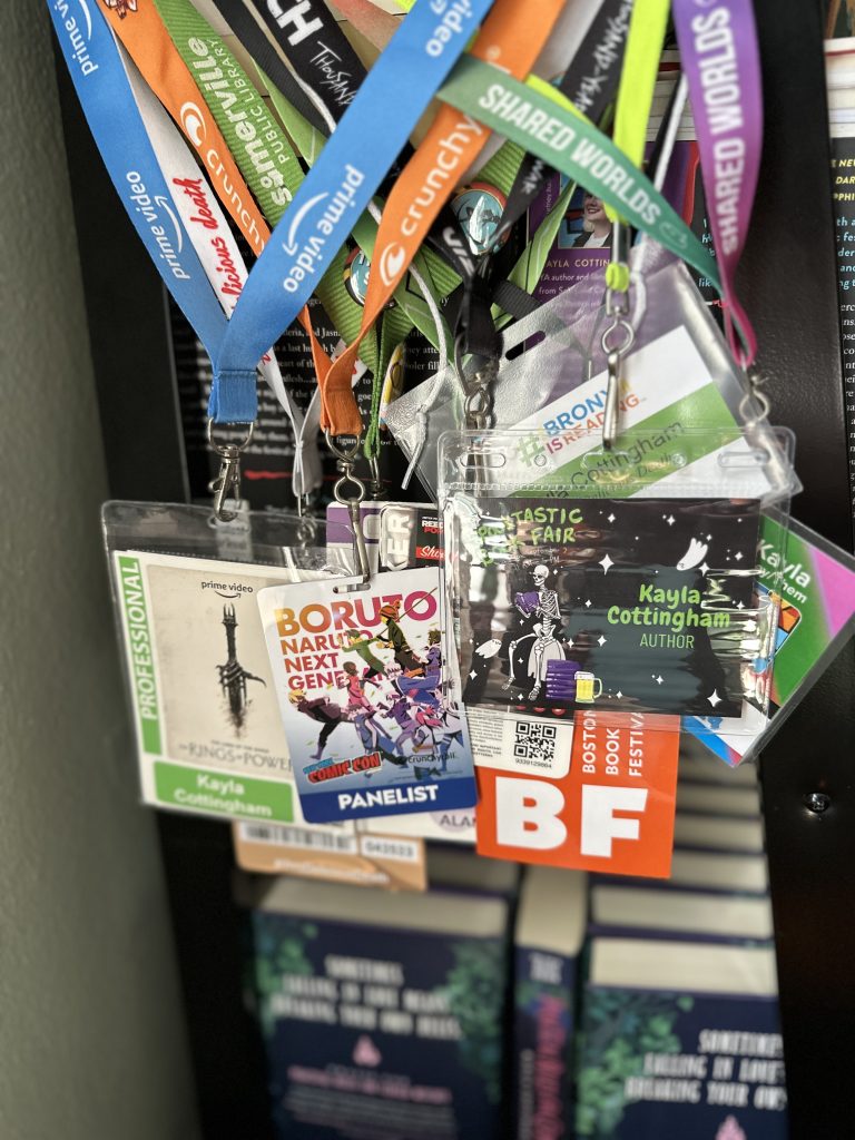Photo of an area of Kayla's bookshelf that shows a collection of lanyards from different events.
