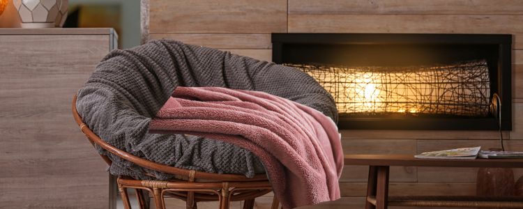 a papasan chair with a pink knit blanket in front of a fake fire place.