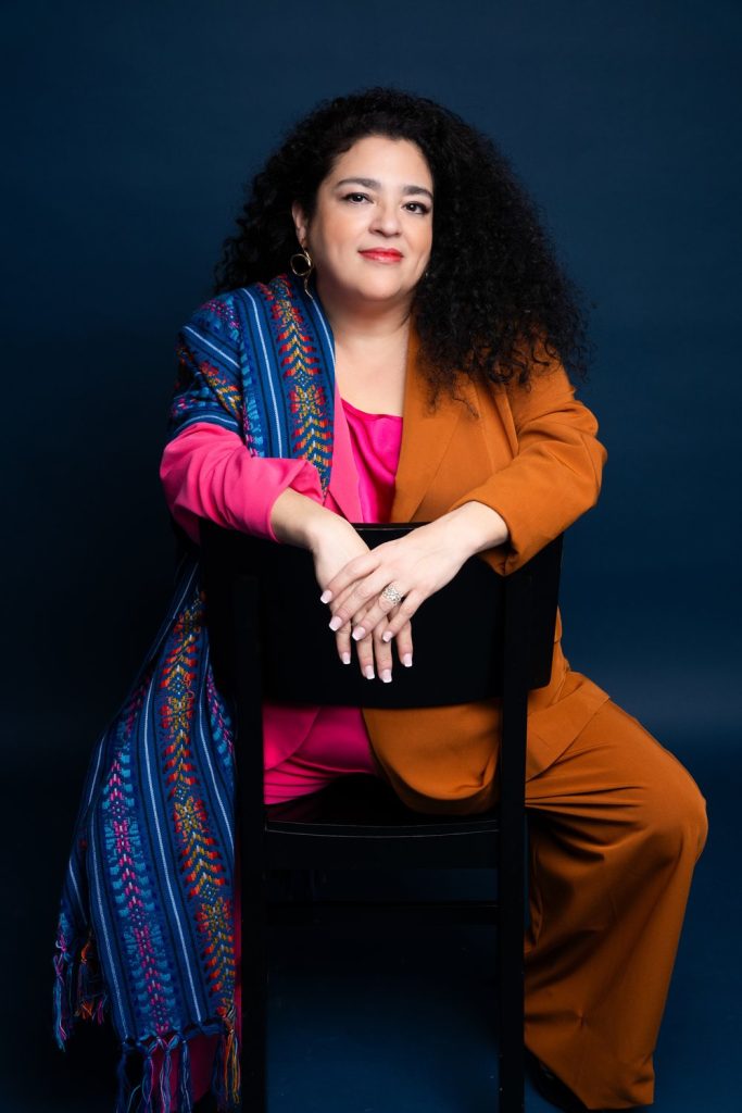Marcela Fuentes sitting backwards on a chair and smiling.