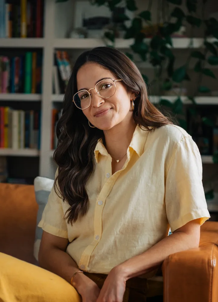 Melissa Mogollon sitting on a couch and leaning on one arm while smiling.
