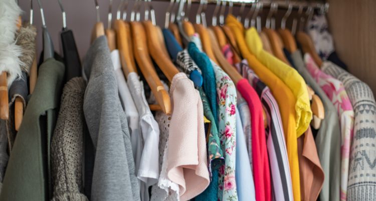 Two dozen colorful pieces of clothing are hung on a rack with wooden hangers.