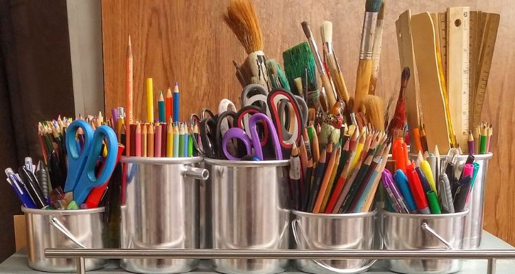 Crafting supplies- scissors, colored pencils, markers, paint brushes and rulers are kept in silver containers.